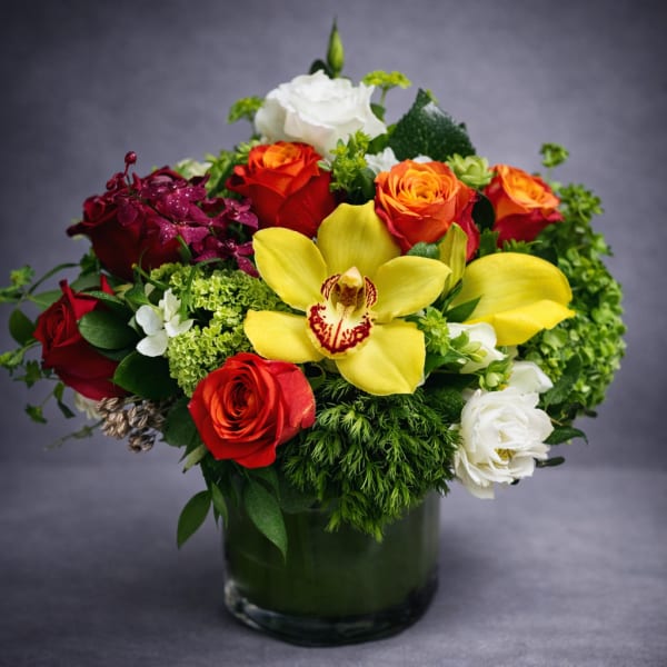 Mixed bouquet in a glass vase with yellow orchid, red and orange roses, and white blooms