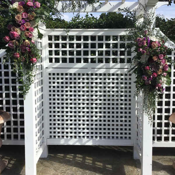 Floral arrangements of pink and purple roses on a white pergola arch