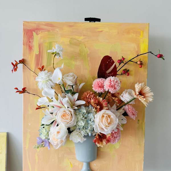 Mixed floral arrangement in a blue pedestal vase against a painted backdrop