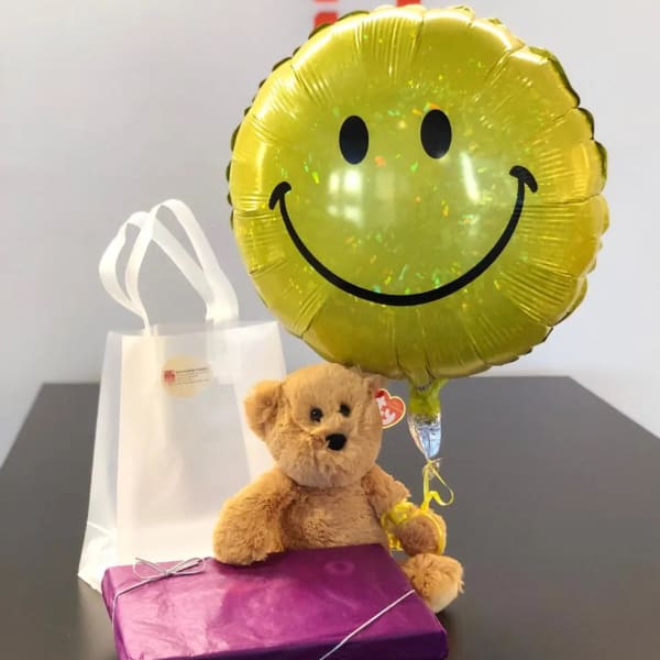 Teddy bear with a smiley balloon, gift bag, and wrapped box