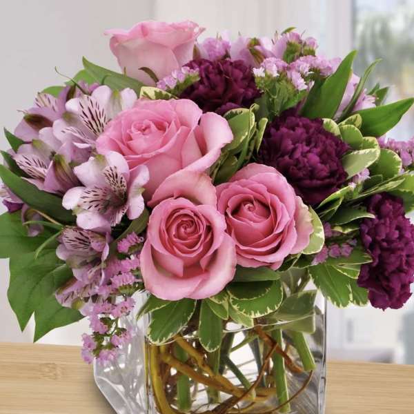 Pink roses and purple flowers arranged in a clear square vase