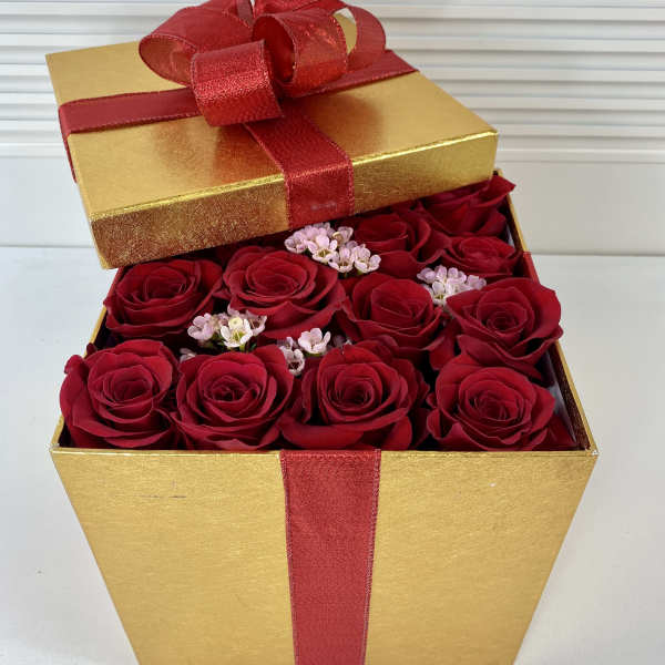 Gold gift box filled with red roses and small pink flowers