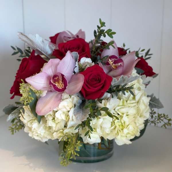 Bouquet of red roses, pink orchids, and white hydrangeas in a glass vase