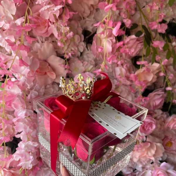 Clear gift box with pink roses, red ribbon, and a small crown