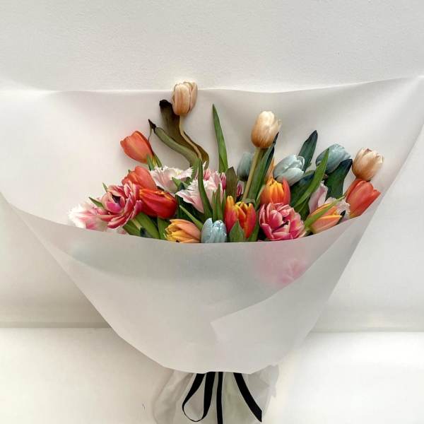 Mixed tulip bouquet wrapped in white paper with a black ribbon