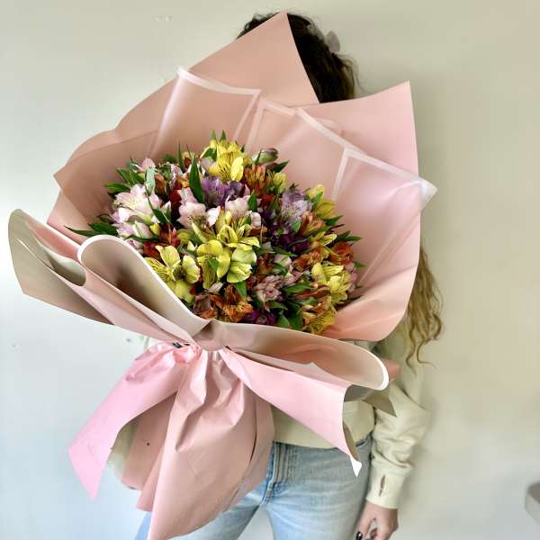Person holding a large bouquet of multicolored flowers wrapped in pink paper