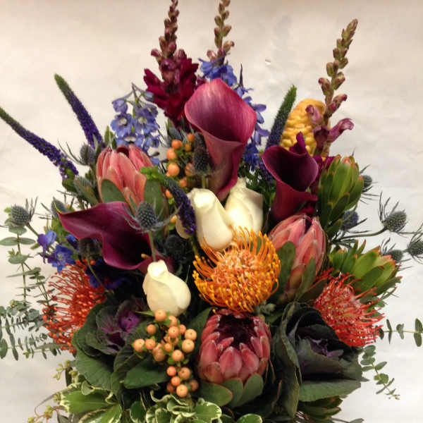 Mixed bouquet with calla lilies, protea, and purple spikes in a wrapped vase