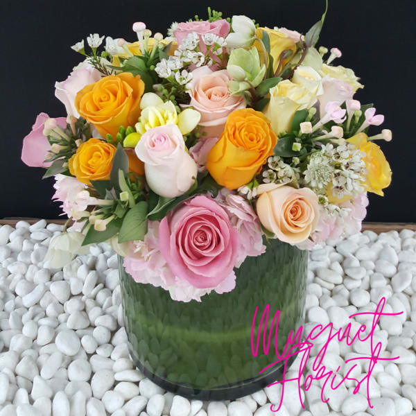 Mixed roses in a green glass vase with white pebbles