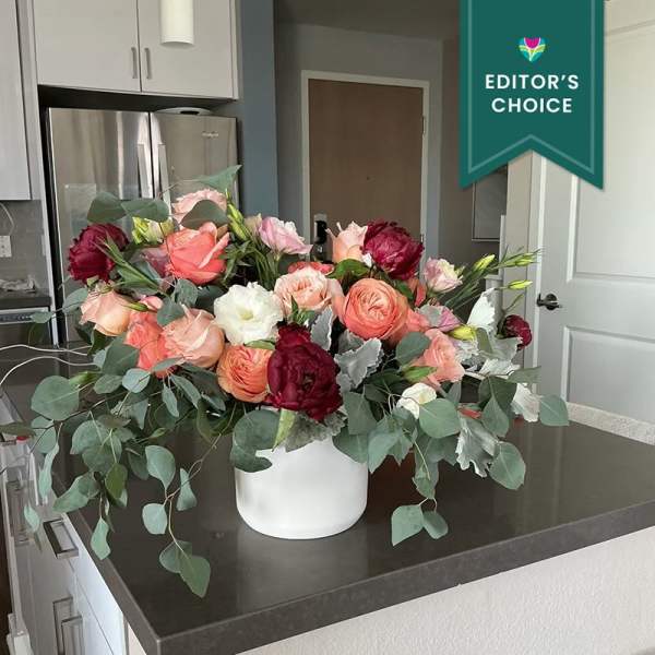 Mixed bouquet of pink, peach, white, and burgundy flowers in a white vase