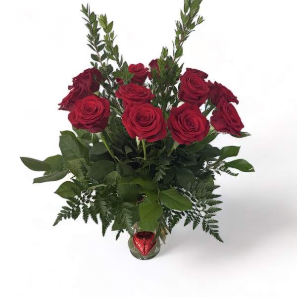 Red roses arranged in a clear glass vase with a red heart ornament