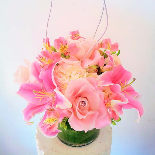 Pink floral arrangement in a glass vase with hanging silver cords