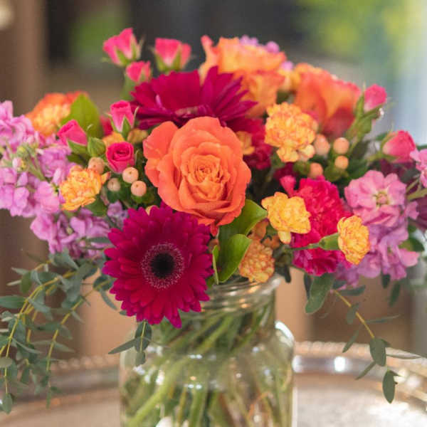 Mixed bouquet of orange, pink, and purple flowers in a glass jar vase