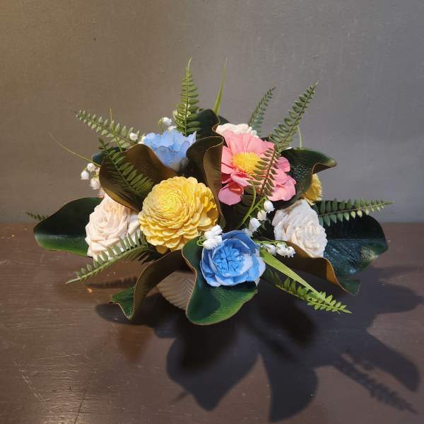 Small bouquet of pastel flowers with dark green leaves in a low container