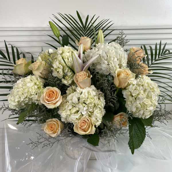 Cream roses and white hydrangeas arranged with lilies in clear wrap