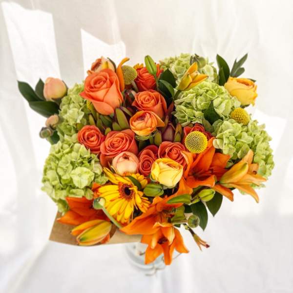 Bouquet of orange roses, lilies, and green hydrangeas in kraft wrap and glass vase