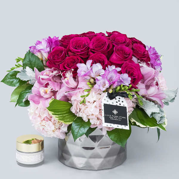 Pink rose and orchid arrangement in a silver vase with a candle beside it