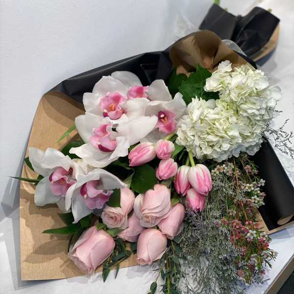 Bouquets of pink roses, white orchids, and white hydrangeas wrapped in black paper