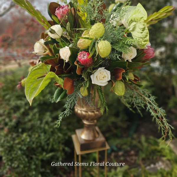 Tall floral arrangement with white roses and pink protea in a gold vase