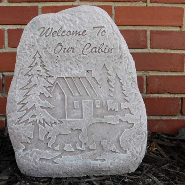 Carved stone plaque with a cabin, trees, and bears against a brick wall