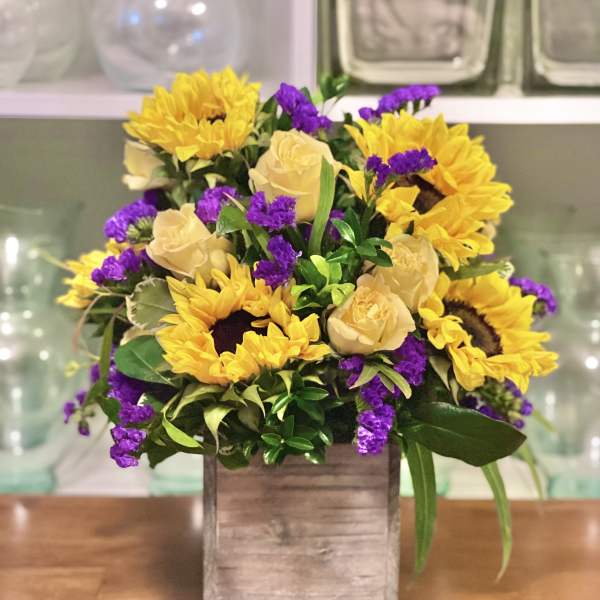 Yellow sunflowers, cream roses, and purple filler flowers in a wooden box