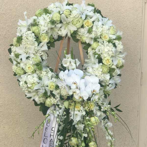 Large white floral funeral wreath on an easel with a ribbon