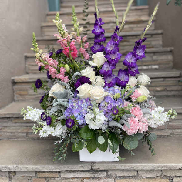 Tall floral arrangement with purple, pink, and white blooms in a white container
