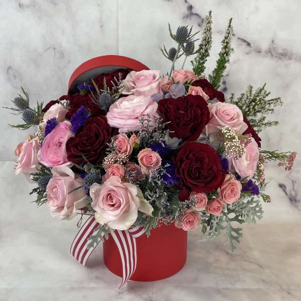 Pink and burgundy rose arrangement in a red hat box with a striped ribbon