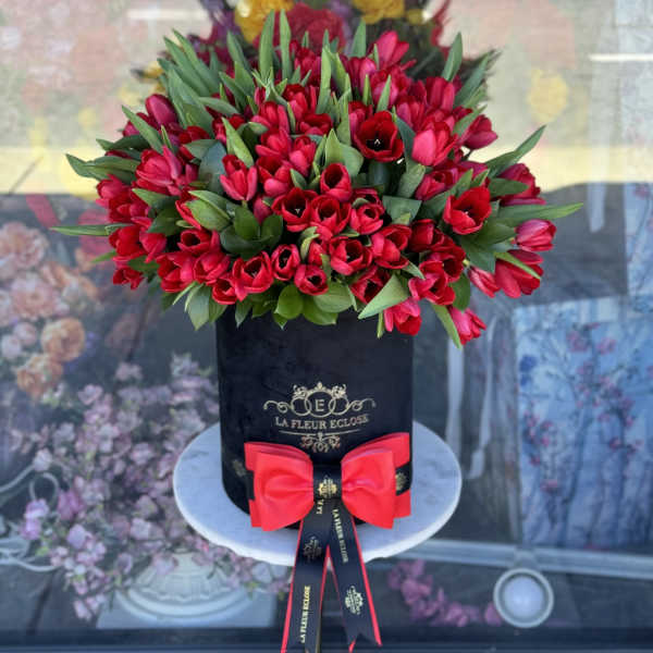 Red tulips arranged in a black hatbox with a pink bow