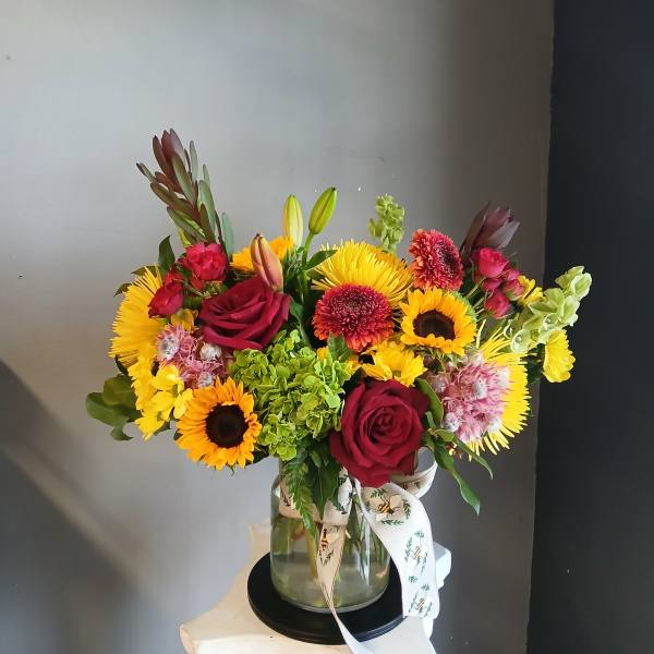 Mixed bouquet of red roses, sunflowers, and yellow blooms in a glass vase