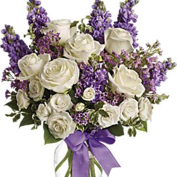 White roses and purple flowers in a clear glass vase with a purple ribbon
