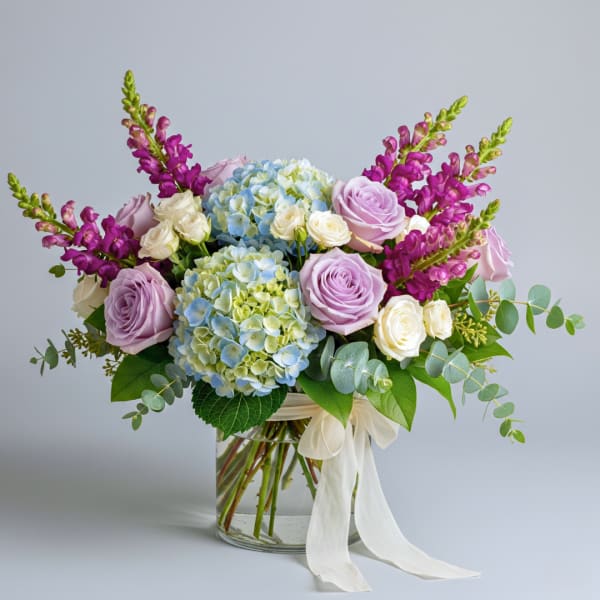 Bouquet of lavender roses, blue hydrangeas, and purple snapdragons in a glass vase