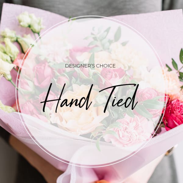 Hand-tied bouquet of pink and white flowers wrapped in pale pink paper