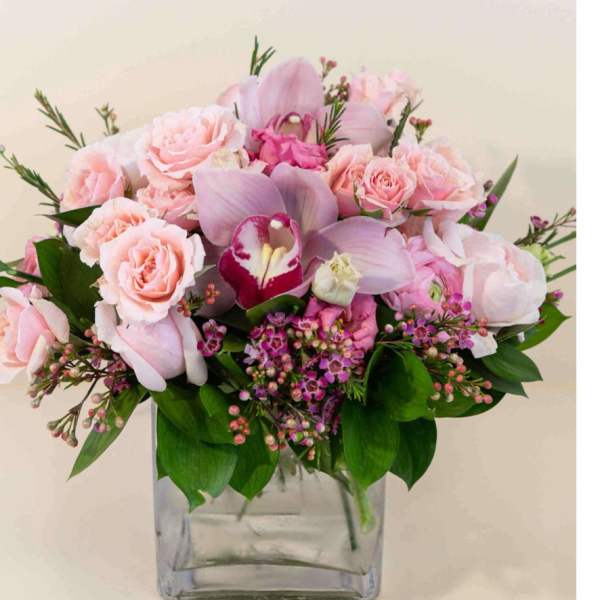Pink roses and orchids arranged in a clear square vase