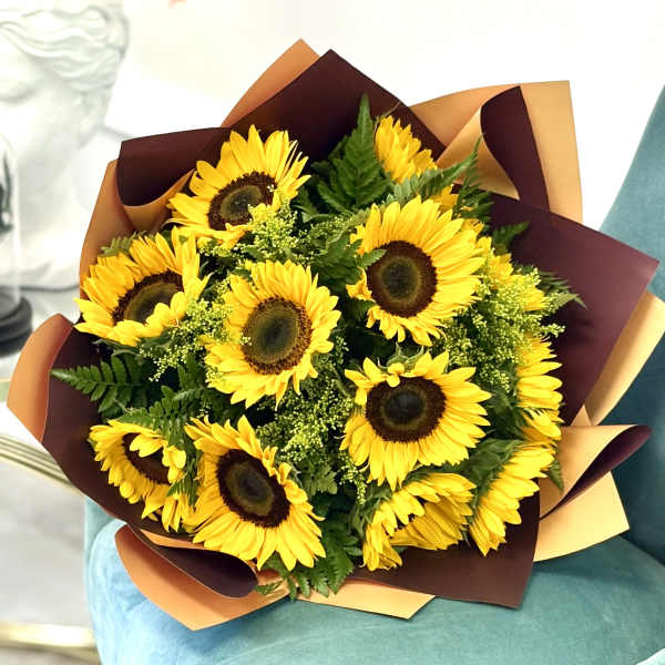 Bouquet of bright yellow sunflowers with greenery wrapped in brown and tan paper on a teal chair