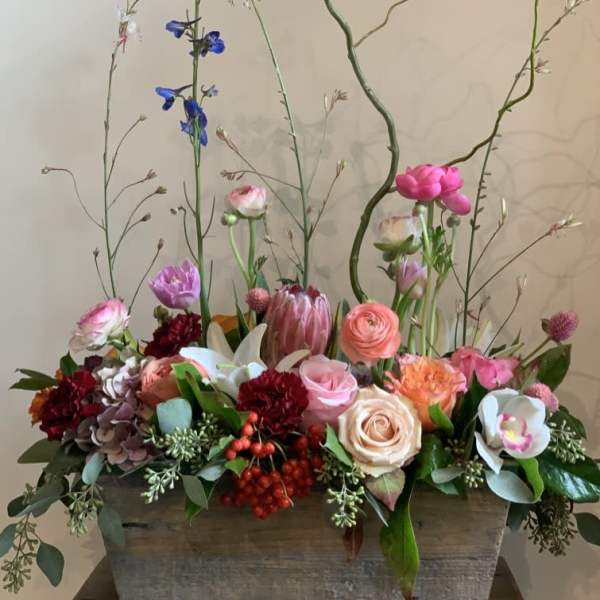 Mixed floral arrangement in a rectangular wooden planter with tall branching stems