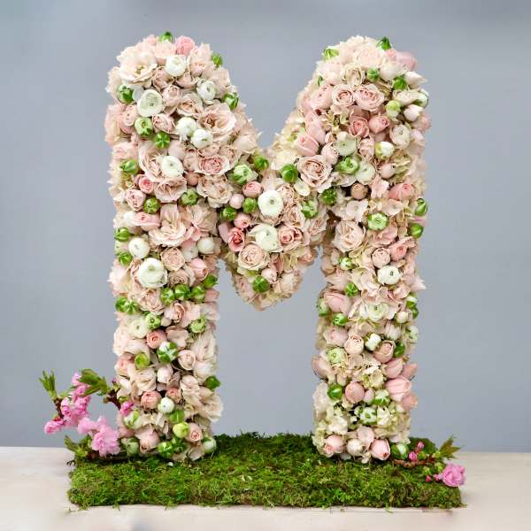 Large floral letter M of blush roses and white blooms on a moss-covered base