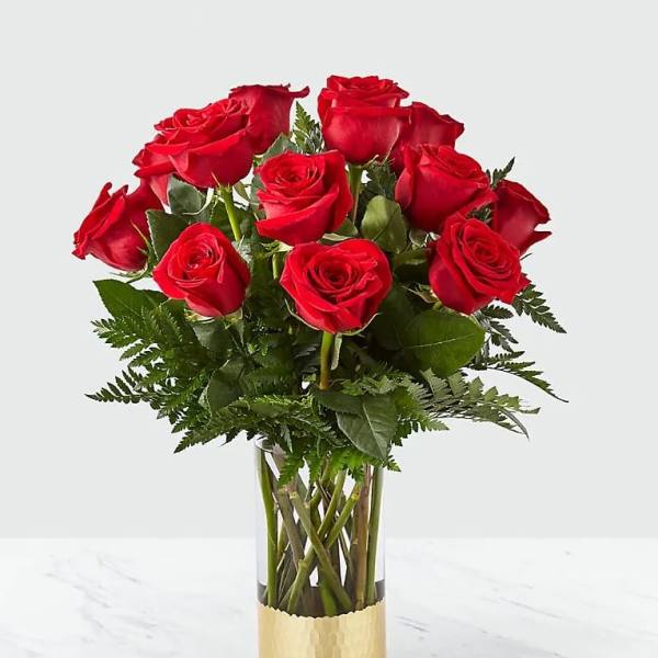 Red roses arranged in a clear glass vase with a gold base