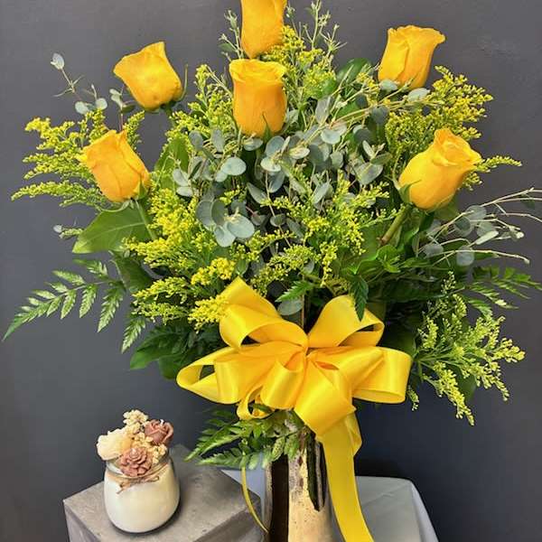 Yellow roses arranged in a tall vase with a large yellow ribbon
