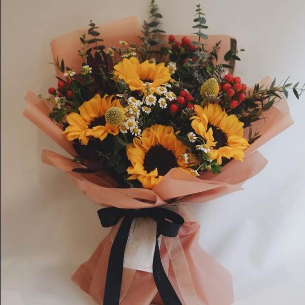 Bouquet of sunflowers with small white daisies and red berries wrapped in peach paper