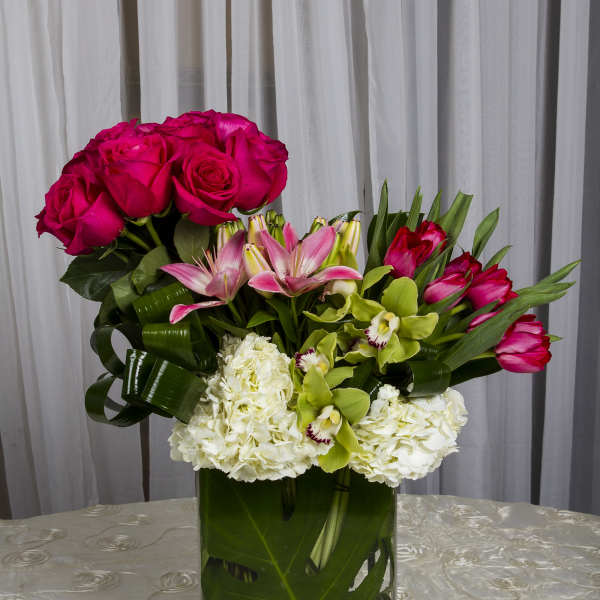 Pink roses, lilies, orchids, and white hydrangeas in a glass vase