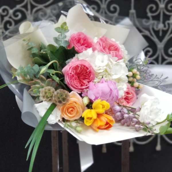 Mixed bouquet of pink, white, yellow, and peach flowers wrapped in paper