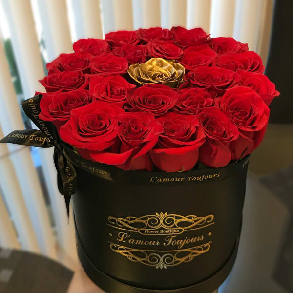 Round black hat box filled with red roses and a single gold rose in the center.