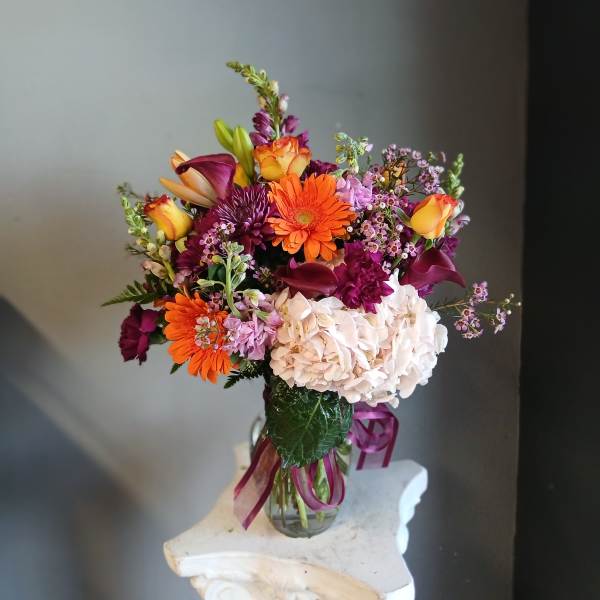 Mixed bouquet of orange, purple, and white flowers in a glass vase