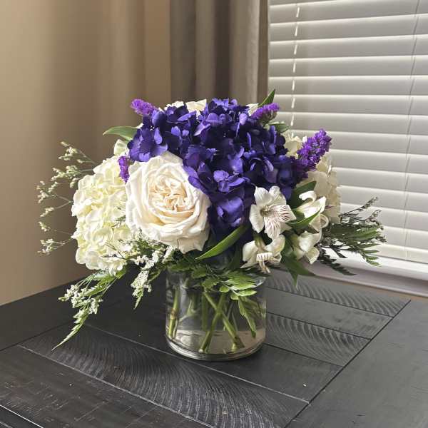 Purple and white floral arrangement in a clear glass vase