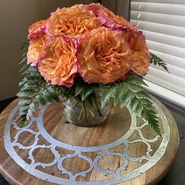 Orange and pink roses in a clear glass vase with fern foliage