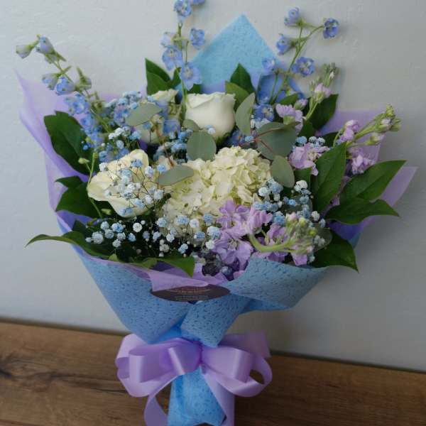 Bouquet of white and lavender flowers wrapped in blue paper with a purple ribbon