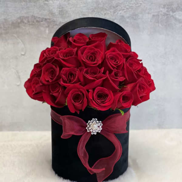 Red roses arranged in a black hatbox with a burgundy ribbon
