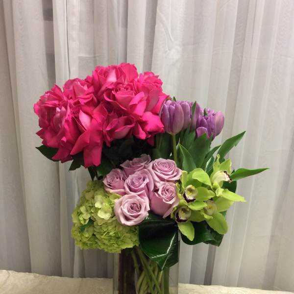 Pink roses, lavender roses, tulips, hydrangea, and green orchids in a glass vase