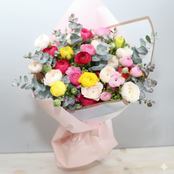 Hand-tied bouquet of pink, red, yellow and cream ranunculus wrapped in pale pink paper