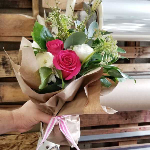 Hand-tied bouquet of pink and white roses wrapped in brown paper